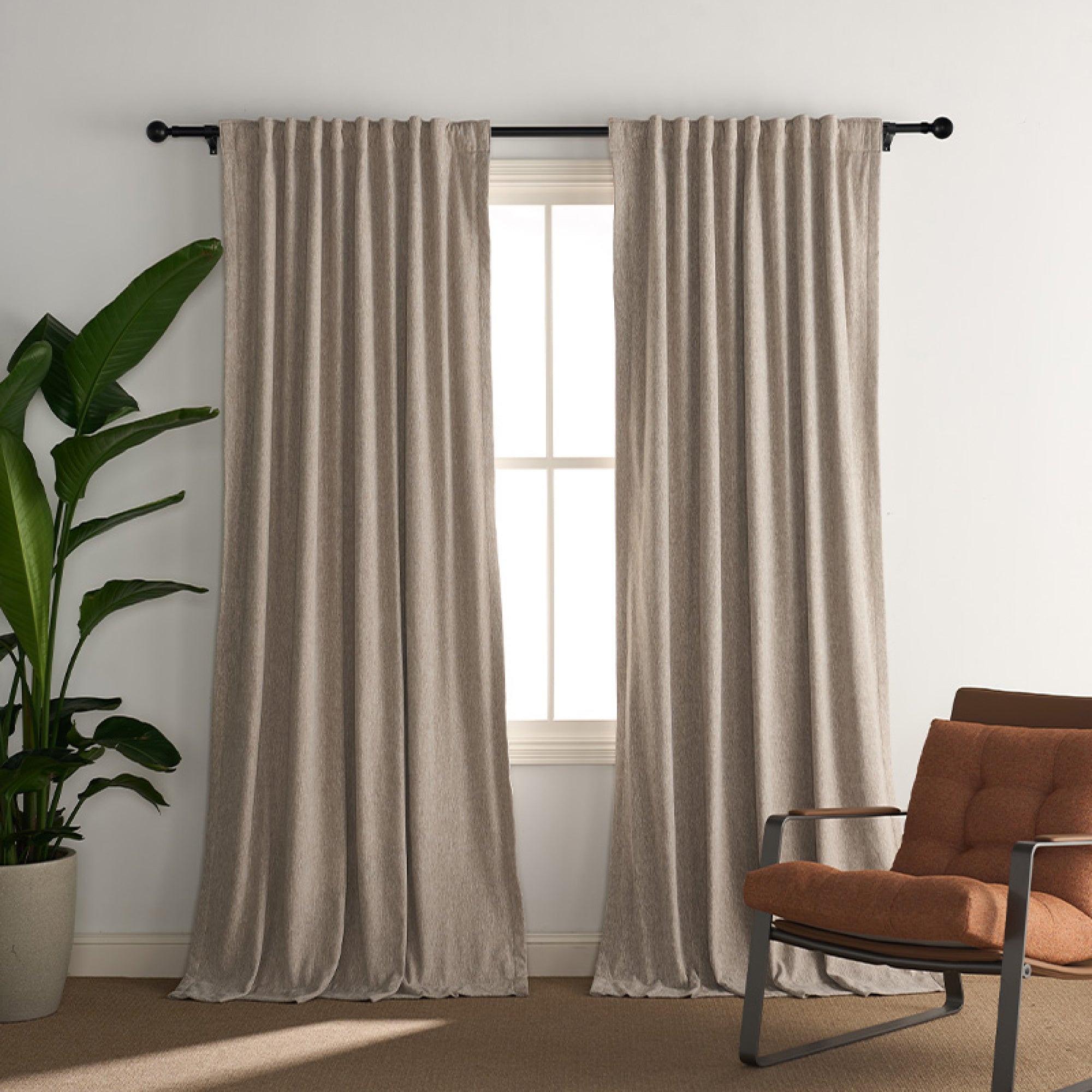 Custom black curtain rod with Roman round finials holding tailored beige curtains in a contemporary room setting.