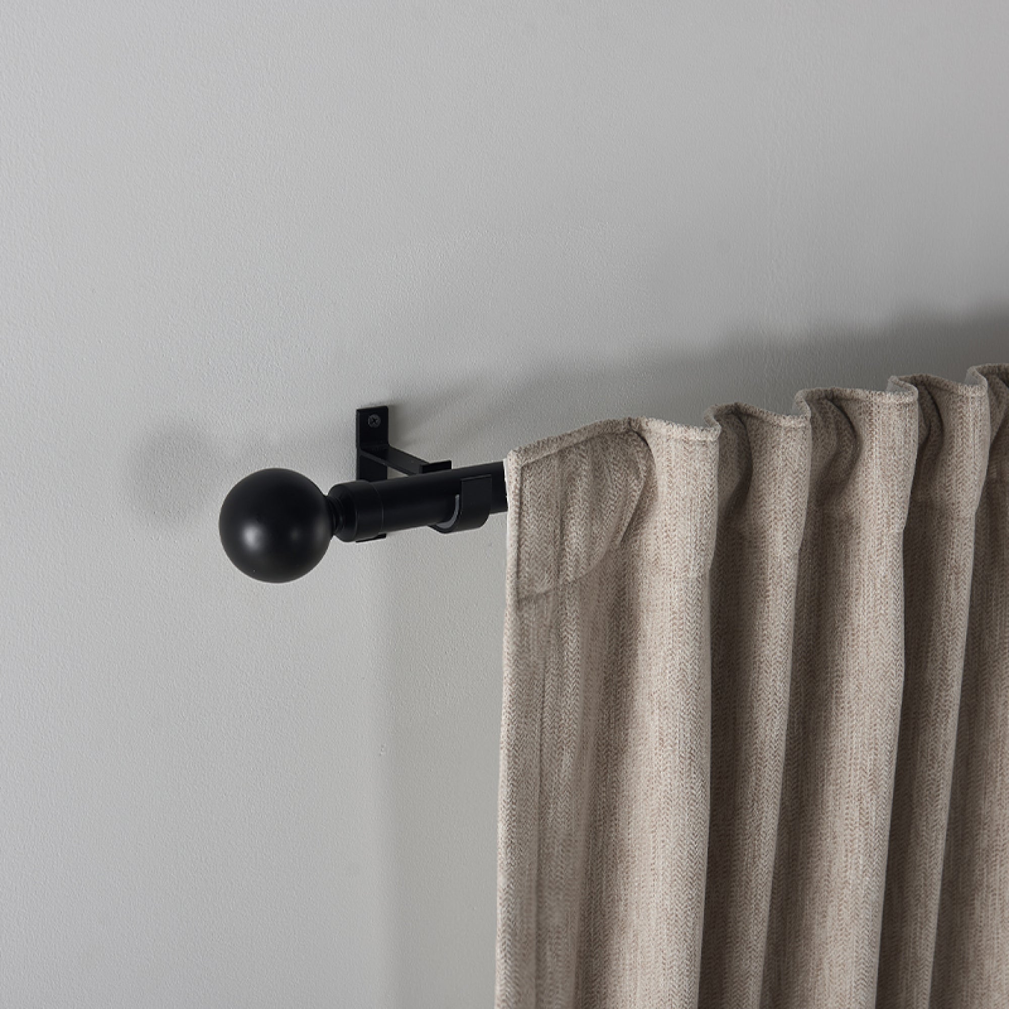Black Roman round finial curtain rod installed on a wall, holding a textured beige outdoor curtain.