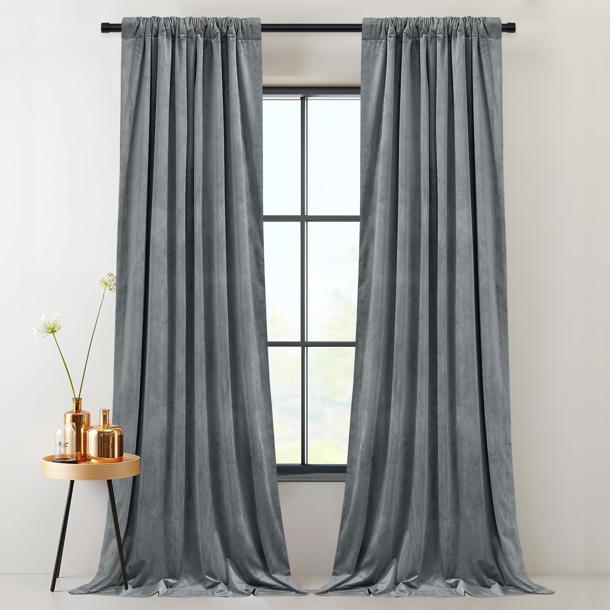Two grey velvet thermal insulated light blocking thick drapes on a rod pocket, framing an indoor window with a side table.