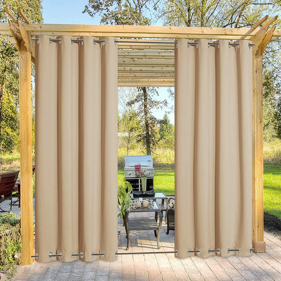 Two beige blackout outdoor curtains with stainless top & bottom grommets on a wooden patio pergola, providing windproof shade.