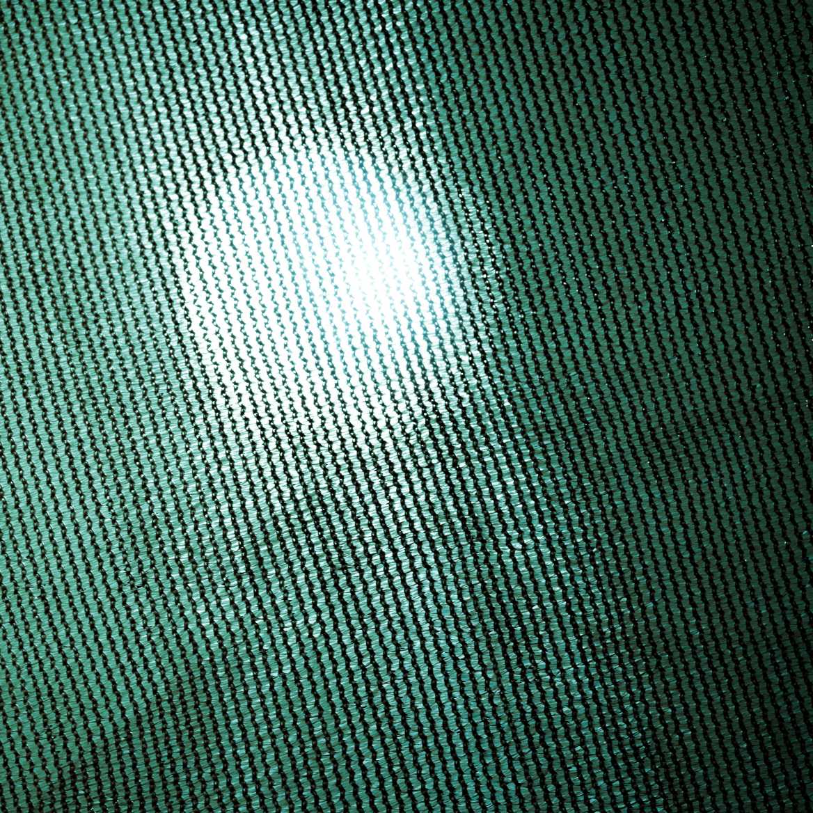 Detailed close-up of teal green breathable HDPE sun shade sail fabric, showing its UV block weave with sunlight filtering through.