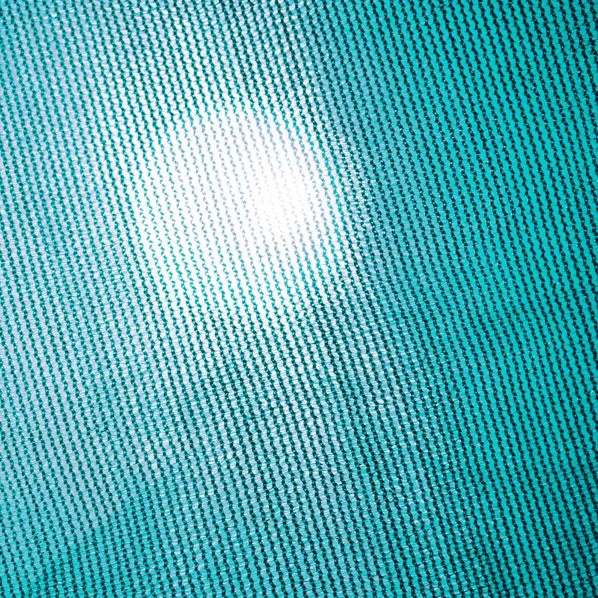 Close-up of breathable teal HDPE sun shade sail fabric with light filtering through its UV block mesh texture.