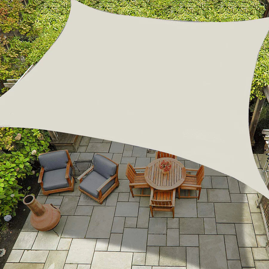 Beige waterproof rectangle sun shade sail providing sun protection over an outdoor patio with wooden dining set and lounge chairs.