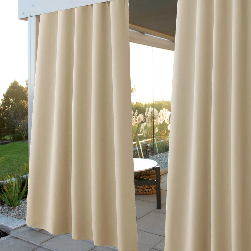 Beige waterproof grommet top outdoor curtains creating a private patio oasis, seen with a table and garden beyond.