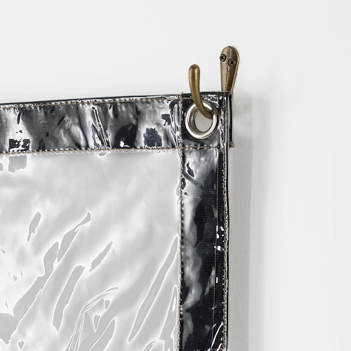 Antique brass single wall hook fastened to a wall, supporting a clear outdoor curtain with a reinforced grommet.