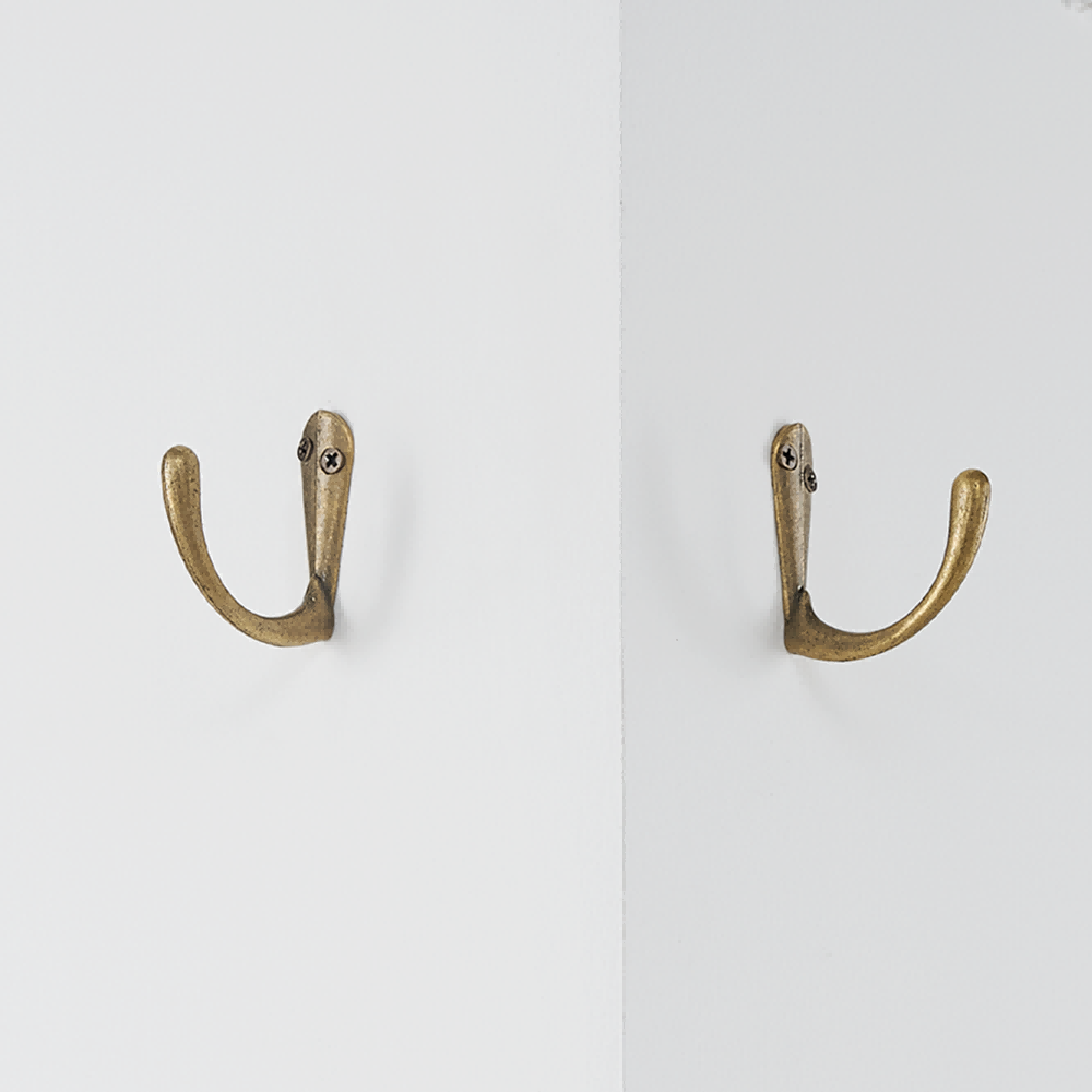 Two antique brass single wall hooks, each securely screwed into a white wall, highlighting their durable metal construction.