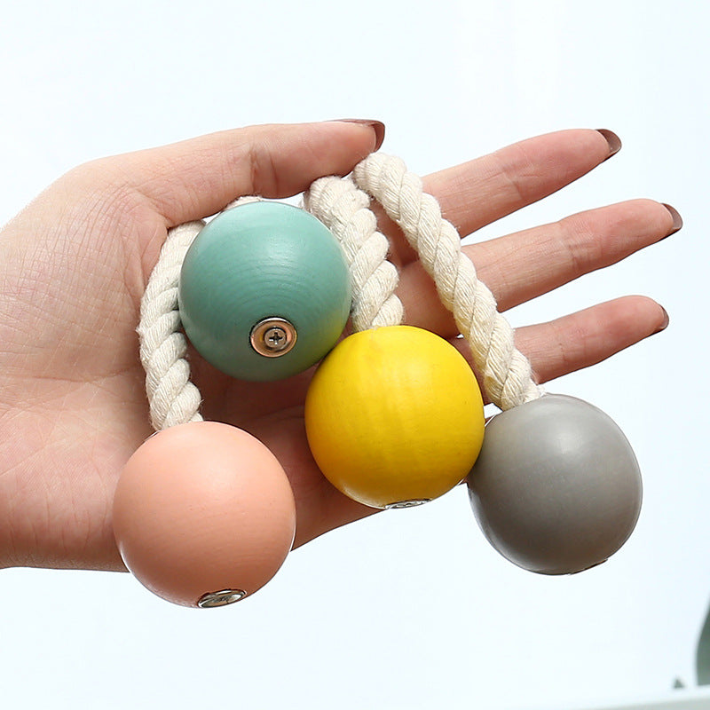 Hand holding four colorful magnetic curtain tiebacks, cotton hand-woven rope holdbacks with wooden balls (teal, yellow, grey, peach).