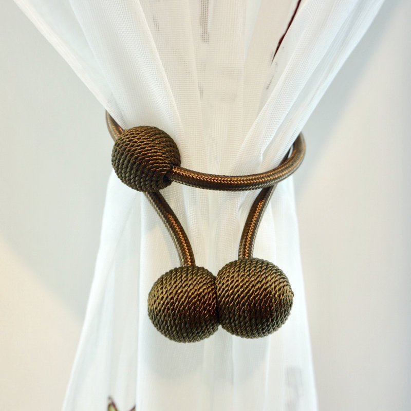 Modern bronze braided magnetic curtain tieback with ball ends, neatly gathering a white sheer curtain. Simple curtain strap design.