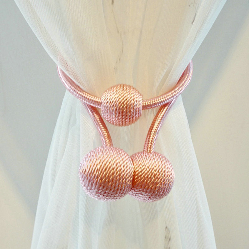 Modern pink braided magnetic curtain tieback straps with decorative spheres, elegantly securing a sheer white curtain.