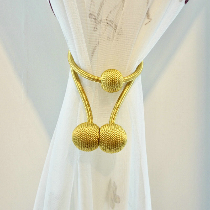 Simple, modern gold magnetic curtain tieback with textured spherical ends, neatly holding back a white outdoor living curtain.
