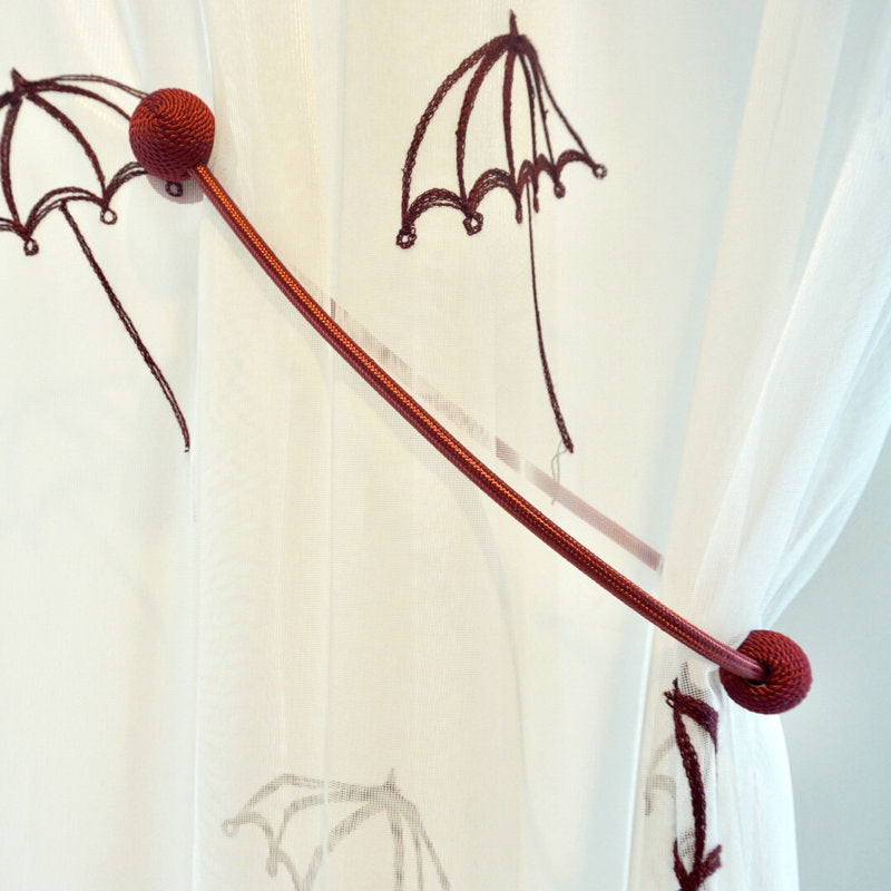 Modern red braided magnetic curtain tieback securing a sheer white curtain with subtle brown umbrella patterns for a chic look.