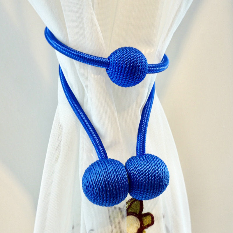Vibrant blue magnetic curtain tieback strap with three woven spheres holding a white sheer curtain. Modern home decor.