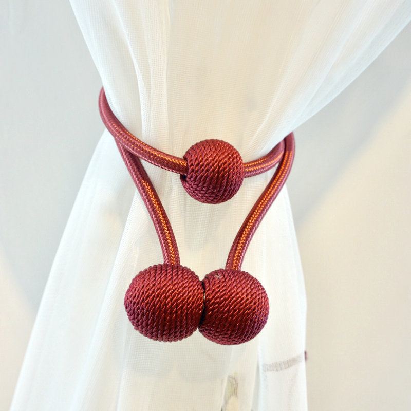 Simple modern burgundy magnetic curtain tieback straps with textured balls securing a sheer white curtain.