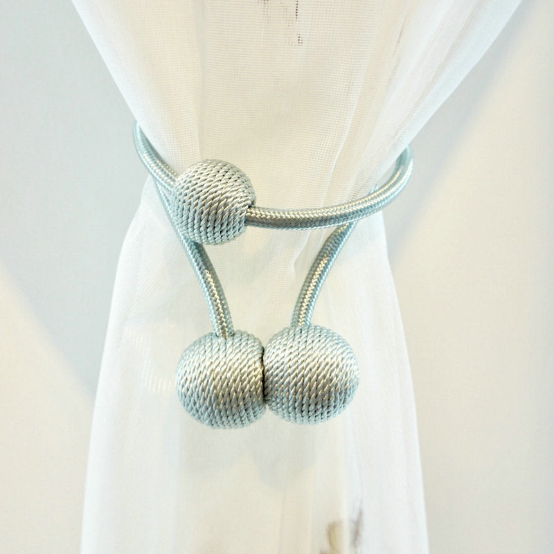 Simple silver magnetic curtain tieback with woven ball design, securing a white sheer outdoor curtain.