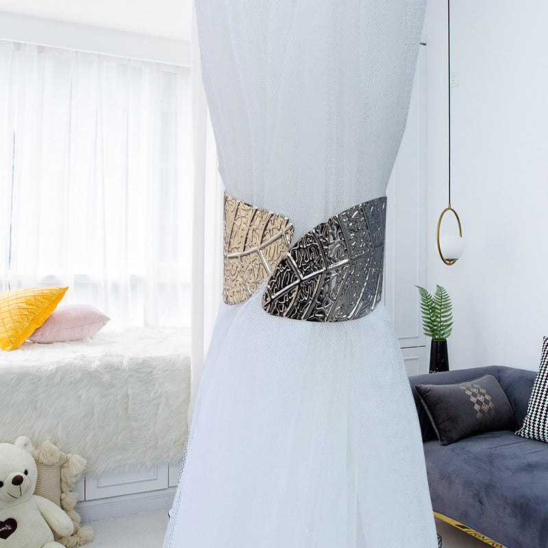 Gold and silver metallic angel wings curtain tieback, featuring a textured leaf design, holding back a sheer white curtain.