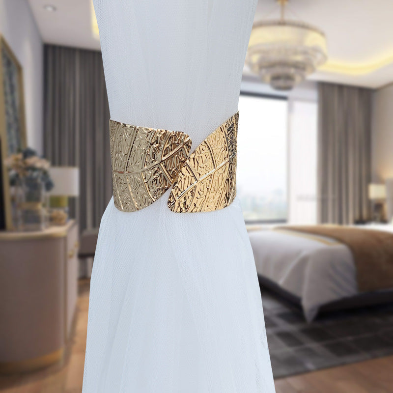 Decorative gold angel wings curtain tieback with leaf pattern securely holding a white sheer window curtain.