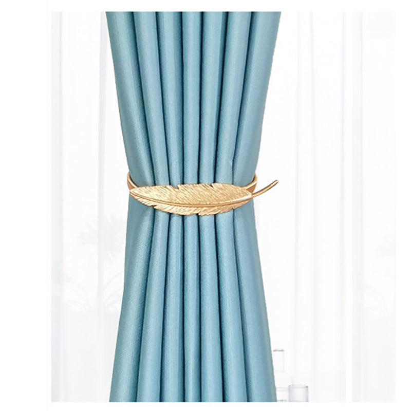 Gold feather design metal curtain tieback holding a pleated blue outdoor curtain