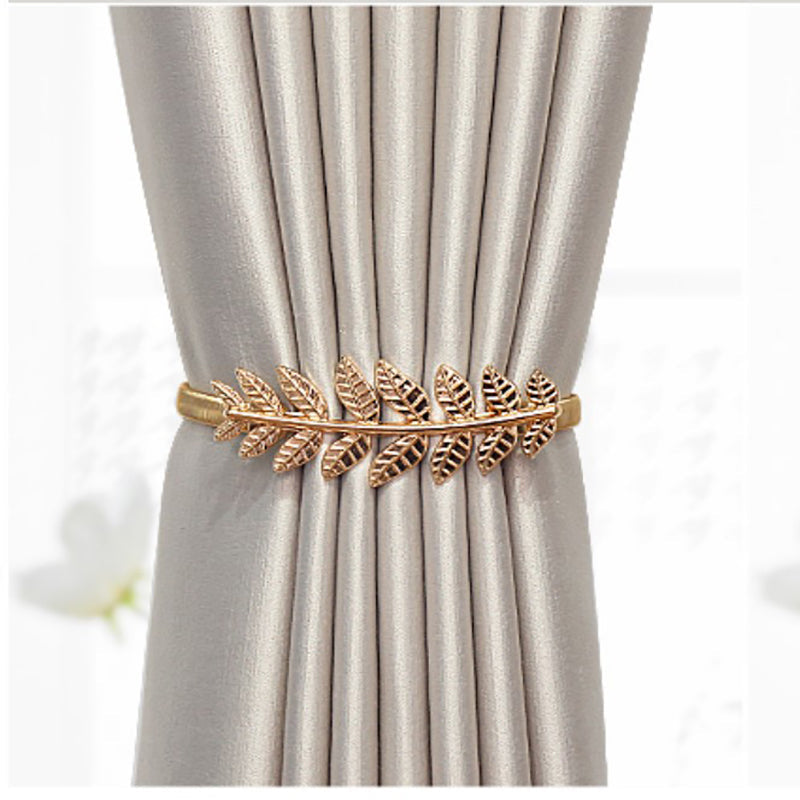 Decorative gold metal leaf design curtain tieback holding a gathered beige window curtain. Ideal for blackout or sheer curtains.