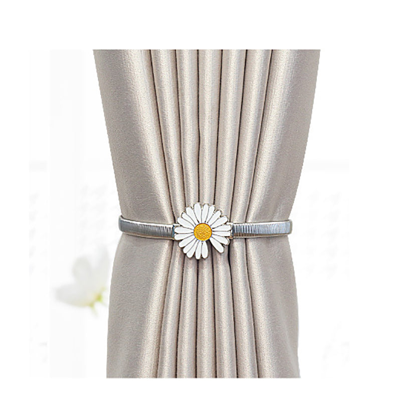 Silver metal curtain tieback with a white daisy flower, securing a pleated light beige outdoor curtain.