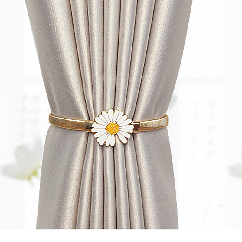 Gold metal curtain tieback with white daisy charm securing a pleated weatherproof grey outdoor curtain.