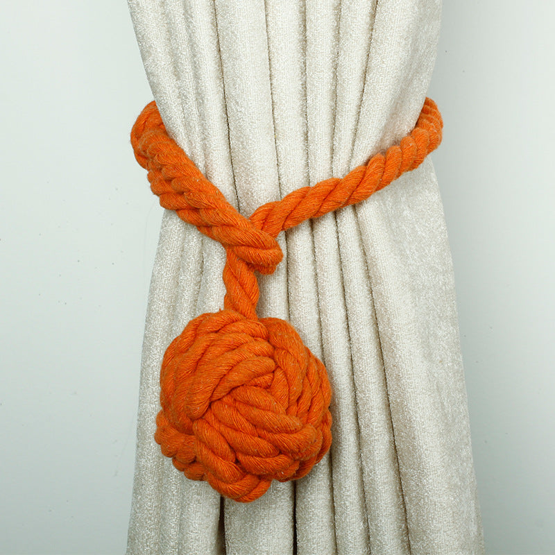Orange macrame rope curtain tieback with a decorative knot, cinching a light outdoor patio curtain, perfect for shade solutions.