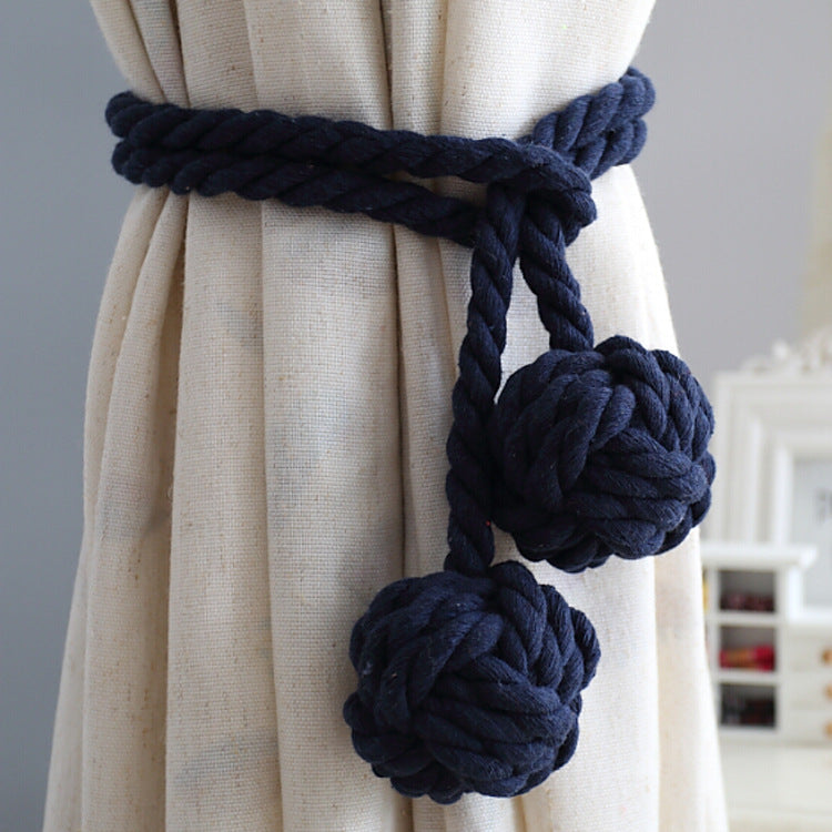 Dark blue nautical rope curtain tieback with decorative monkey knot balls holding back a cream outdoor curtain.