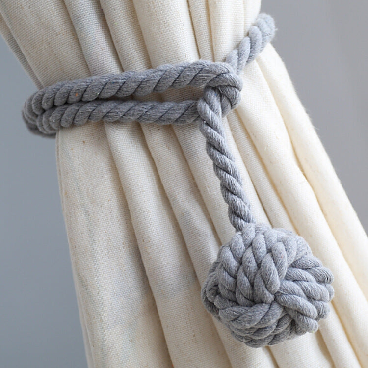 Gray macrame rope curtain tieback with decorative knot securing a pleated beige weatherproof outdoor curtain. Ideal for patio.