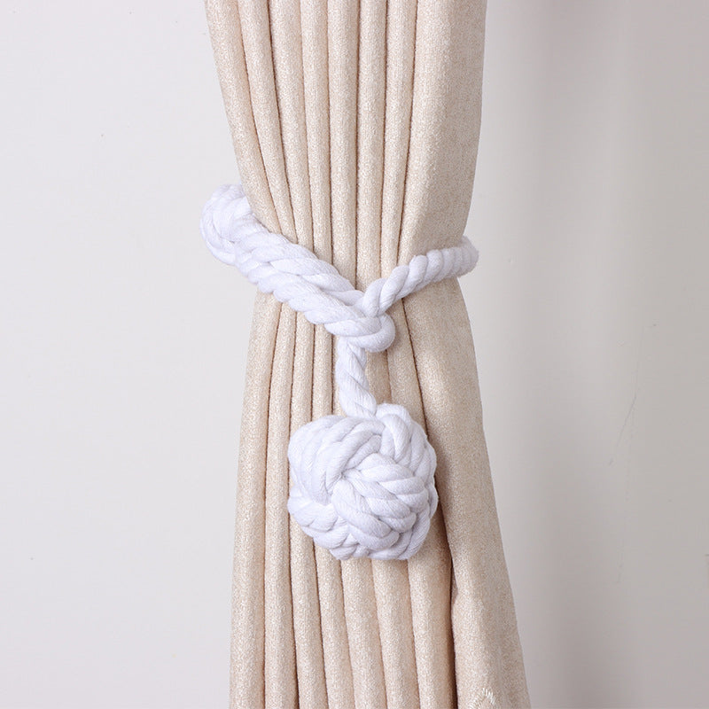 White macrame curtain tieback with a monkey fist knot, securing a pleated beige outdoor curtain.