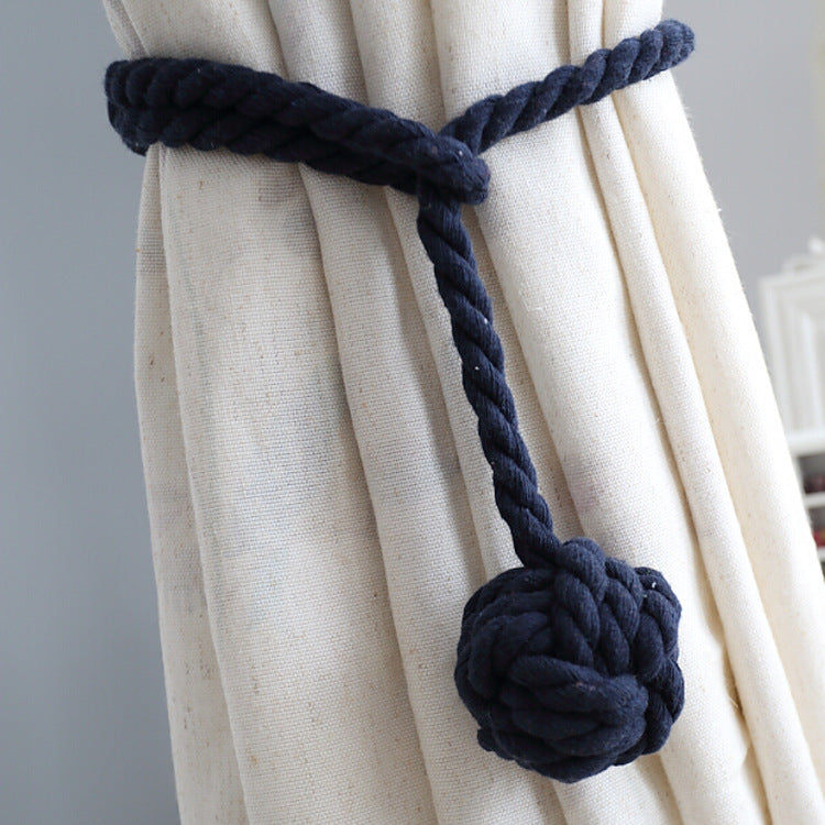 Dark blue macrame style rope curtain tieback with a decorative knot, securing a cream outdoor privacy curtain.