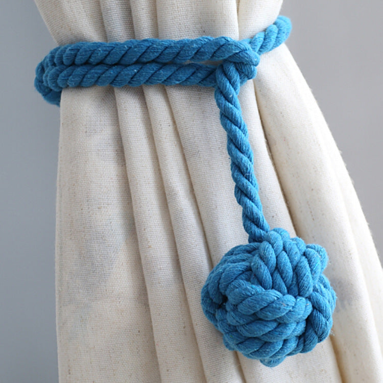 Blue macrame rope outdoor curtain tieback, featuring a decorative knot, cinching a textured beige patio curtain.