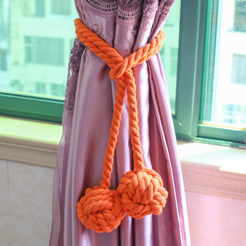 Heavy orange macrame rope tieback with decorative knot ends securing a purple outdoor curtain.