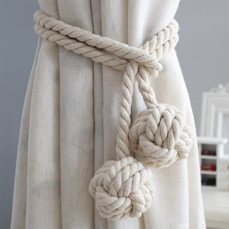 Macrame-style cotton rope tieback with two decorative knot balls securing a light cream curtain. Perfect for outdoor patio decor.
