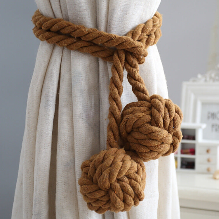 Macrame style curtain tieback with thick brown braided rope & two decorative knot balls, holding a light outdoor curtain.