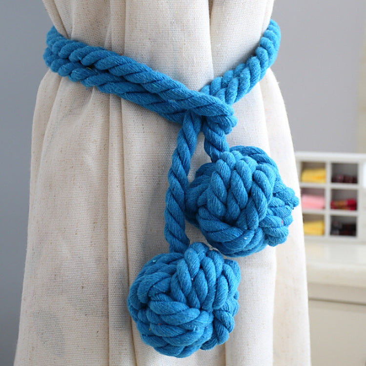 Stylish blue rope curtain tieback securing a neutral outdoor patio curtain, with two decorative braided knot accents.