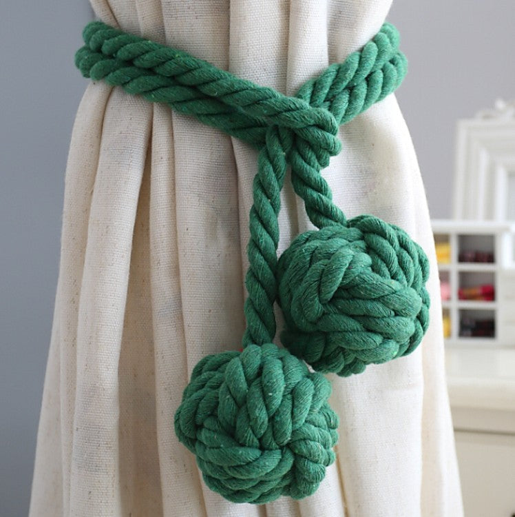 Thick green rope curtain tieback securing a beige outdoor curtain, adorned with two decorative monkey fist knots.