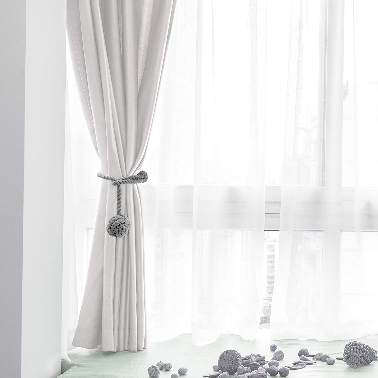 Grey macrame curtain tieback with a decorative knot holding a white curtain open by a bright window.