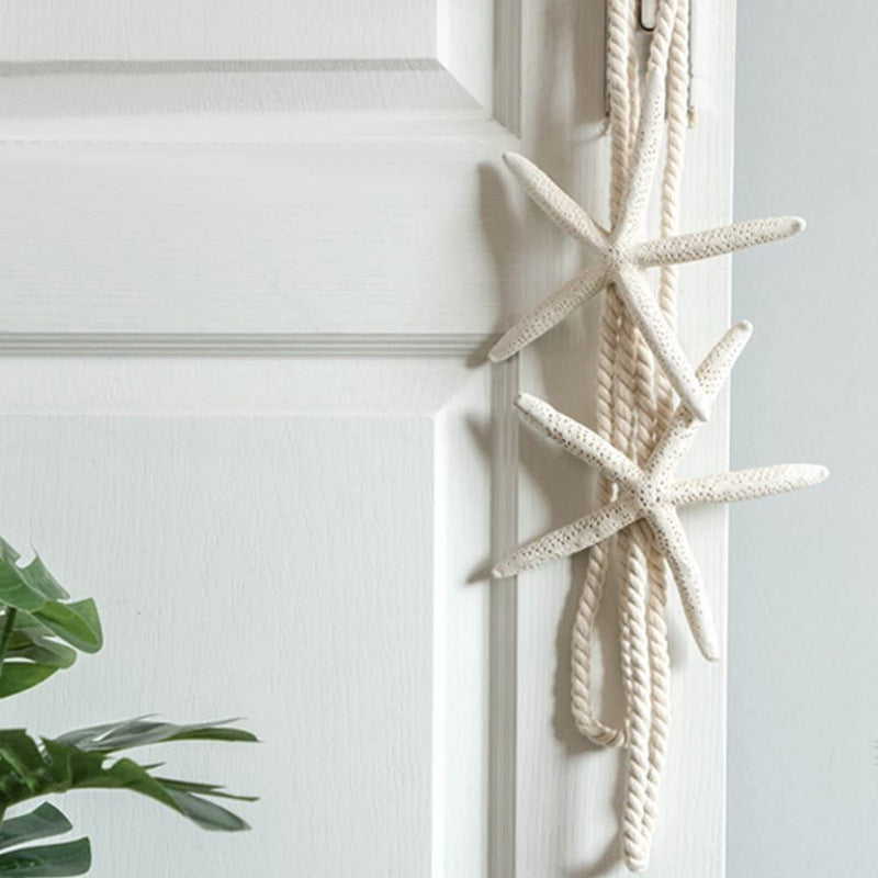 Two natural white starfish on a braided rope curtain decoration strap tieback, hanging on a white paneled door for coastal style.