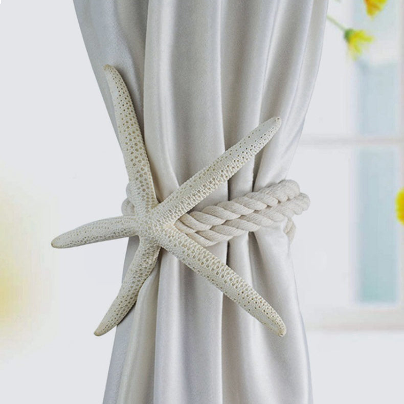 Natural starfish and nautical rope curtain tieback elegantly holding a white outdoor curtain. Perfect for beach or coastal decor.