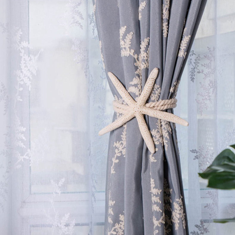 Elegant natural starfish curtain decoration strap tieback with rope detail, securing a blue outdoor curtain with white botanical patterns.
