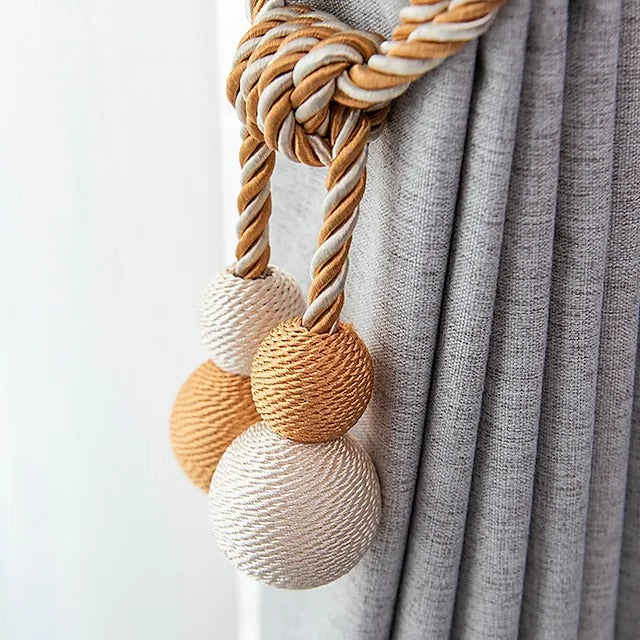 Elegant braided beige & gray magnetic ball tieback holding a textured gray outdoor curtain. Perfect window treatment accessory.