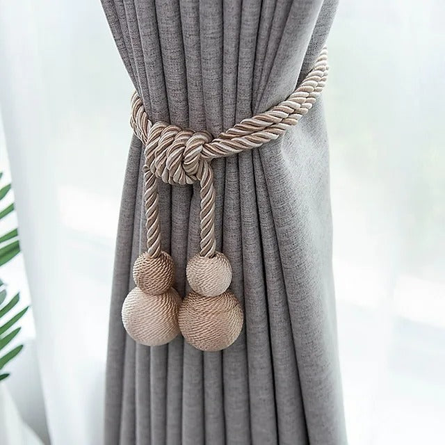 Beige & white twisted rope magnetic ball tieback securing a grey pleated curtain as a stylish window treatment.