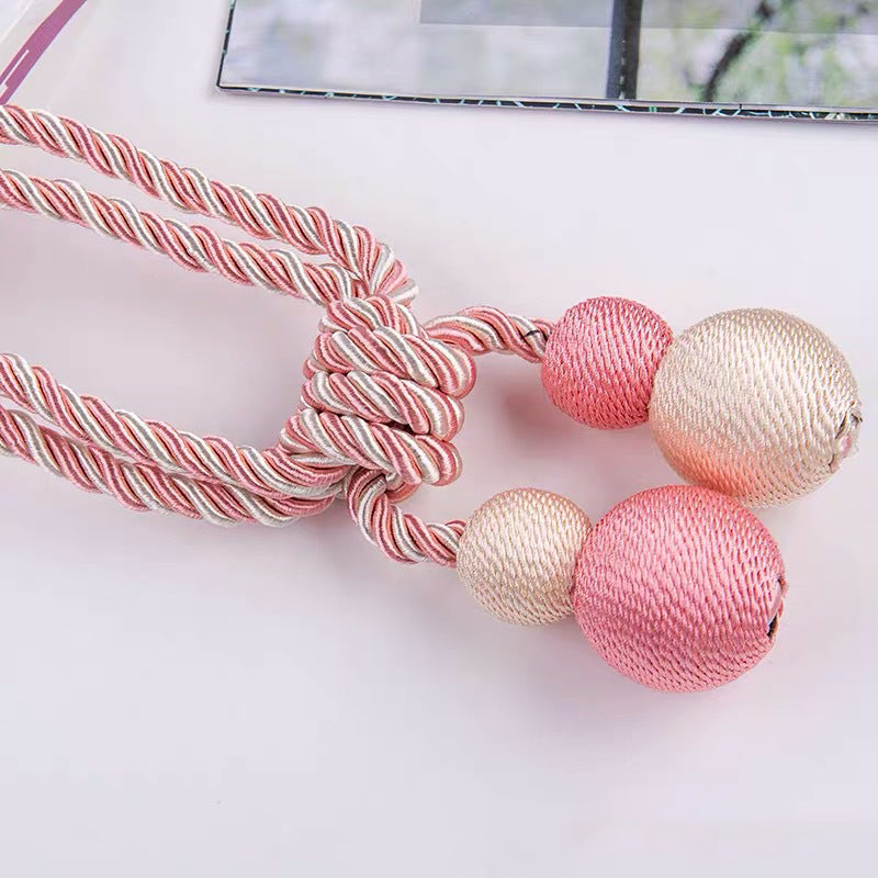 Pink, white, gray braided magnetic curtain tieback featuring decorative pink and light gold balls for window treatments.