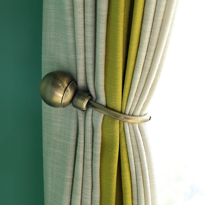 Bronze U-shaped curtain buckle hook tieback securing cream and green outdoor curtains against a teal wall.