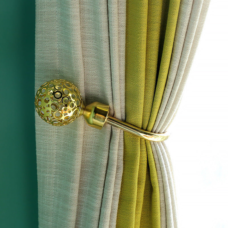 Decorative gold U-shaped hollow spherical curtain tieback securing beige and green window curtains.