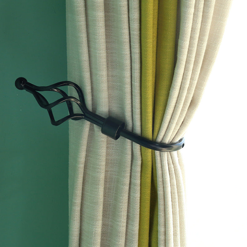 Decorative black metal U-shaped hollow curtain buckle hook tieback holding beige and green drapes on a teal wall.