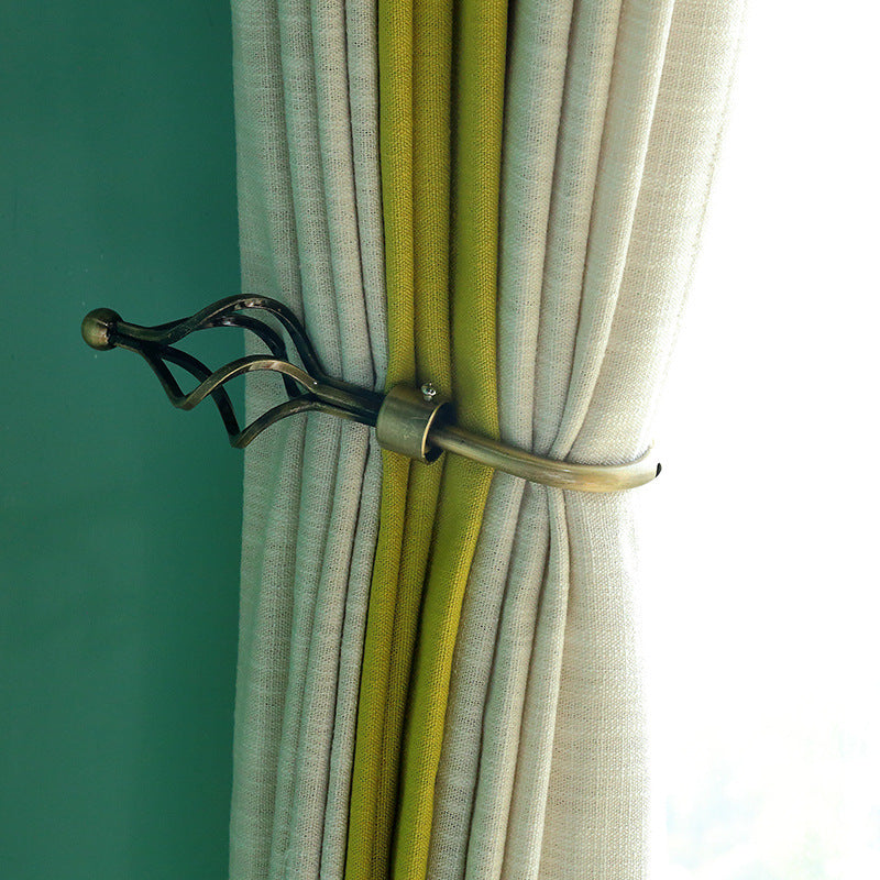 Close-up of a decorative antique brass U-shaped hollow curtain tieback holding pleated grey and lime green outdoor curtains.