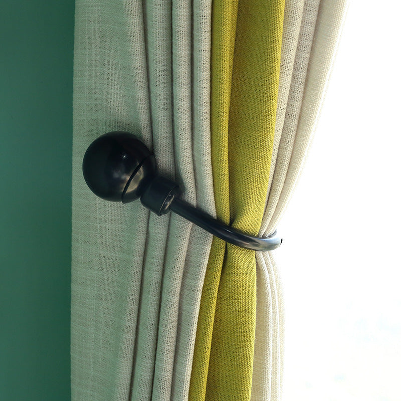 Black U-shaped hollow curtain buckle hook tieback securely holding pleated cream and lime green outdoor curtains.