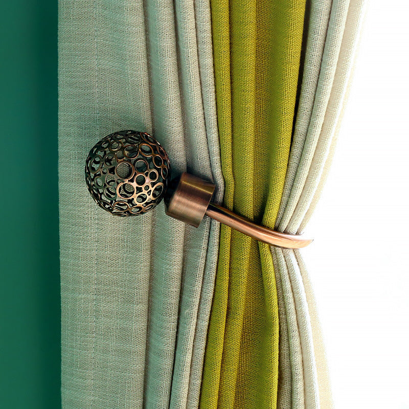 Bronze U-shaped hollow curtain buckle hook tieback with a unique perforated sphere design, securing pleated green & cream outdoor curtains.
