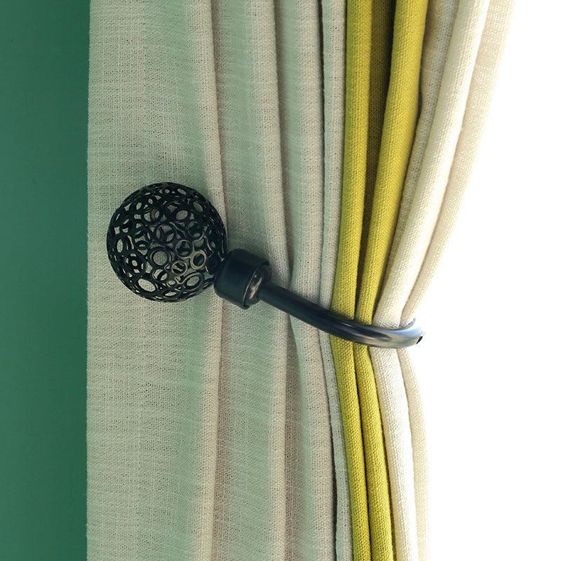 Decorative U-shaped black hollow spherical curtain tieback holding beige and lime green outdoor curtains for patio or pergola