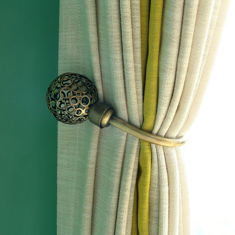 U-shaped antique bronze hollow curtain buckle hook tieback with ornate sphere design holding a light outdoor curtain.
